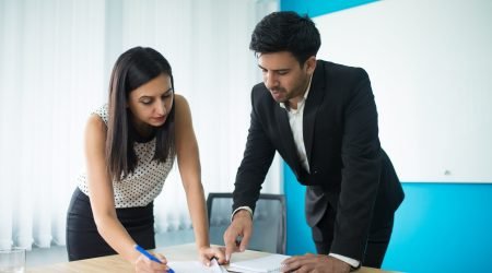 Serious businessman and businesswoman signing contract in boardroom. Young Caucasian female secretary showing papers to executive. Partnership concept